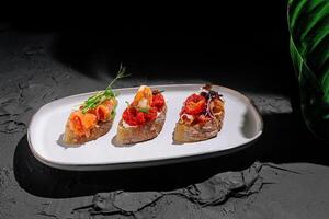 Three gourmet tapas served on rustic bread with vibrant toppings in a stylish setting photo