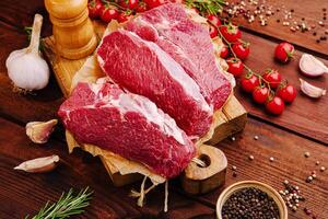 Fresh cuts of beef on a wooden board with herbs and garlic in a rustic kitchen setting photo