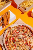 Delicious pizza with toppings served alongside crispy fries and chicken tenders on a vibrant orange background photo