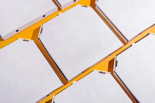 Empty pizza boxes arranged in a geometric pattern on a bright yellow surface photo