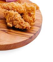 Crispy fried chicken served on a wooden platter with fresh tomato slices and a refreshing dip photo