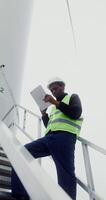 A power plant worker in work gear uses a tablet with a serious look while standing on the steps near the entrance to an industrial wind generator, vertical , bottom view. in 4k, red komodo video