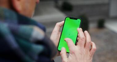 A warmly dressed man uses a phone with a green screen, swiping his finger across the screen, close-up, top view from behind the man's shoulder. Chroma key, mockup. in 4k, red komodo video