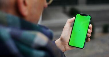grisalho homem usando Móvel telefone com verde tela batendo dele dedo através a tela para a lado, irreconhecível pessoa, topo Visão a partir de atrás a do homem ombro. dentro 4k, vermelho Komodo video