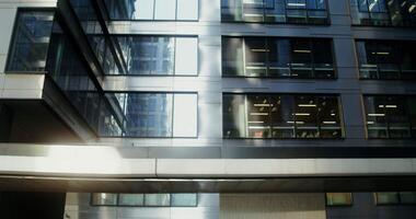 A man with a beard, dressed in casual clothes, uses a mobile walking in courtyard of a modern glass building. transitions from the upper floors of the building to man. in 4k, red komodo video