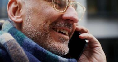 A close-up of the face of a grey-haired, solid man, dressed in a warm scarf, talking on a mobile phone and smiling. in 4k, red komodo video