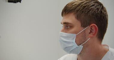 A young male doctor or scientist in a medical mask looks through a microscope while working in a laboratory. in 4k, red komodo. video