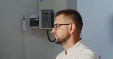 A young man in glasses is a doctor diagnostician in the x-ray room communicates with the patient, preparing for the procedure. Orthopantomography device for teeth, MRI, in 4k, red komodo video