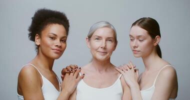Three emotional models of different ethnicity and age group are smiling broadly looking at the camera and at each other. Studio filming against a monochrome background. 4K , red komodo video