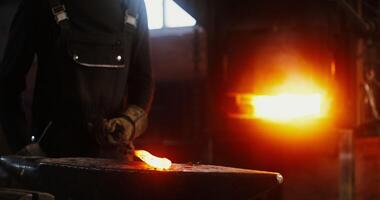 A young blacksmith of African American descent in goggles and equipment works a red-hot iron bar with a hammer to shape the product. in 4k, red komodo video