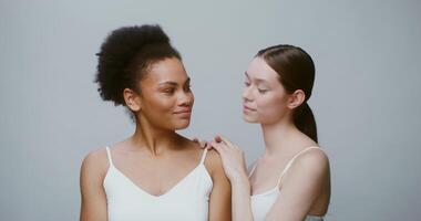 Two young models of different ethnicity posing looking at the camera and smiling. An African-American woman and a woman of European appearance without makeup in the studio. 4K , red komodo video