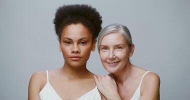 Two models of different ethnicity with a big age difference are smiling, looking at the camera, posing against a solid background in the studio. 4K , red komodo video
