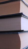 Close-up of a Stack of Colorful Old Hardcover Books in Rays of Sunlight. Camera movement from the bottom. Home collection of books on blurred background. Concept of learning, reading, and knowledge. Vertical video