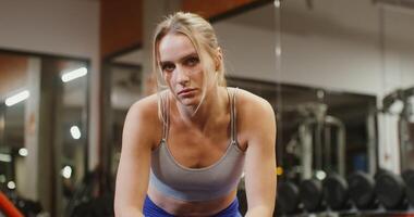 Tired young beautiful woman of european appearance looks directly at the camera leaning on the exercise machine, after training in the modern gym video