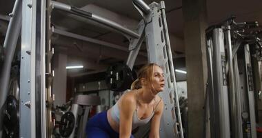 A young woman of European appearance, athletic physique doing bends with a half-squat with a barbell on the exercise machine, doing in the gym. filming from the side, close-up video