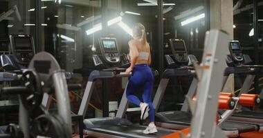 Workout in a well-equipped gym on a modern treadmill with integrated display. Young woman running on a treadmill, view from the back video