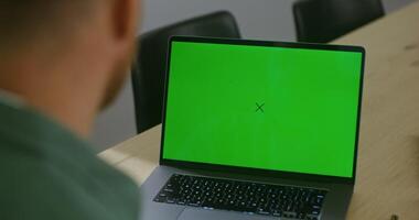 A young fair-skinned man chatting on a laptop with a green screen. Filming from behind, the man's face is not visible, chroma key, copy space video