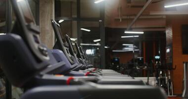 Young woman of European appearance starts training on the treadmill, choosing the training mode and speed, exercising alone in a well-equipped gym, filming from the side video