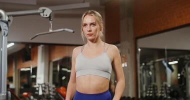 A young beautiful woman of European appearance, dressed in a sports top, does a warm-up in the neck-collar zone before starting exercises on Exercise Machine, close-up video