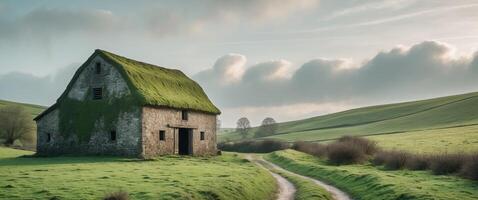 Tranquil rural landscape with stone barn on lush green hills and winding path under cloudy sky photo