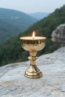 A lit offering candle sits on a rock with a mountain background photo