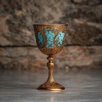 Ornate golden goblet with turquoise inlay against a stone background photo
