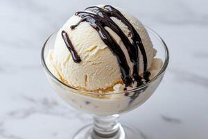 A scoop of vanilla ice cream with chocolate sauce in a glass bowl photo