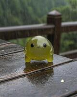 A cute green blob character sits in the rain photo