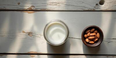 Top view of a jar of almond milk in the center with almonds in a dark bowl positioned to the right on a textured rustic wooden background. photo
