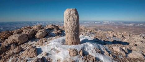 Stone pillar on a snowy mountain peak overlooking a vast landscape photo
