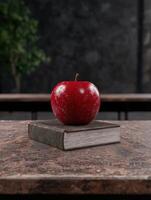 A shiny red apple sits on top of a vintage book photo