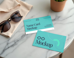 Two teal name card mockups rest on a marble table next to sunglasses and a folded piece of fabric psd