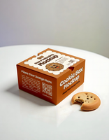 A cookie box mockup sits on a table with a single cookie beside it psd