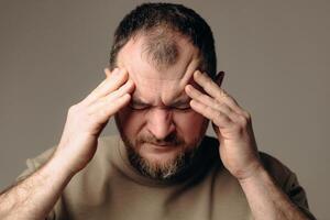 A man has a severe headache. He holds his head in his hands and massages his temples to relieve the pain in his head. Changes in atmospheric pressure affect physical condition and headaches. photo