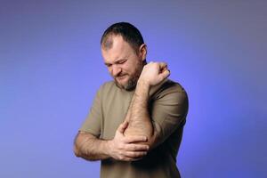 man is experiencing pain in his elbow, expressing discomfort on his face. He is holding joint, demonstrating a problem with arm movement. image illustrates inflammation, injury, or chronic disease. photo