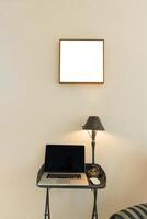 small desk in cozy apartment. There is a modern laptop on the desk. There is a mockup picture on the wall. concept of cozy workspace photo