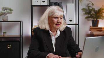 Smiling senior businesswoman using laptop computer and looking at camera at home office table video