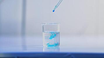 Beaker with water is placed on the laboratory table. A few drops of blue liquid are poured into the water. The examination of diapers process. video