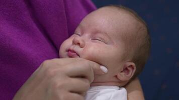 Sleepy newborn kid doesn't want to wake up lying in mum's hands. Mother is touching her baby's plump cheeks trying to wake him up. Close up. video