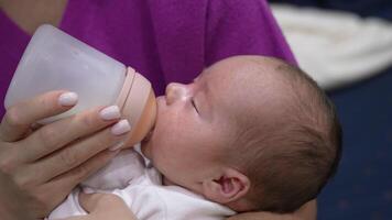 Loving mother holding a baby in her arms and feeding it from the bottle. Newborn child being fed from a bottle with pacifier. Close up. video