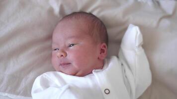 Sweet newborn boy is lying on the bed and turning his little head back and forth. Yawning tiny kid in a white costume. Close-up from above. video