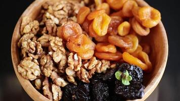 Prunes, dried apricots and nuts in a wooden bowl on a dark background video