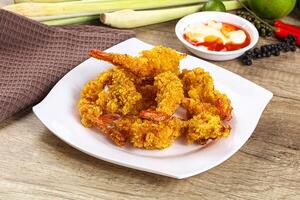A plate of fried shrimp on a table with a bowl of sauce photo