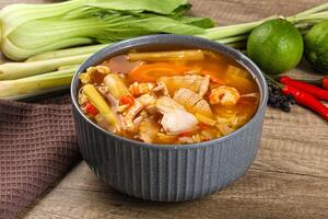 A bowl of soup with vegetables and meat on a wooden table photo