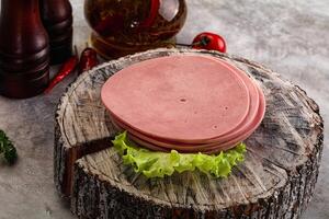 A piece of ham on a wooden block with lettuce and peppers photo
