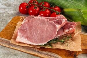Raw pork on a cutting board with tomatoes and corn photo