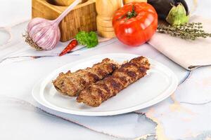 Two meat skewers on a white plate with vegetables photo