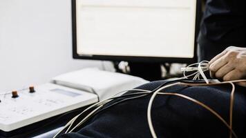 A closeup of biofeedback sensors adhered to a participants skin surrounded by wires and hightech gadgets while a researcher adjusts the settings on a nearby computer screen.. photo