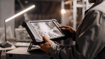 An engineer adjusting settings on a handheld device that syncs with a large holographic display demonstrating seamless integration of various ecosystem components in realtime.. photo