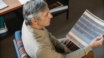 A grayhaired man leans forward in his chair holding a printed report that highlights genetic markers related to aging with notes handwritten in the margins.. photo